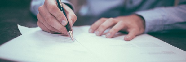 The hands of person in a suit signing a document with a pen