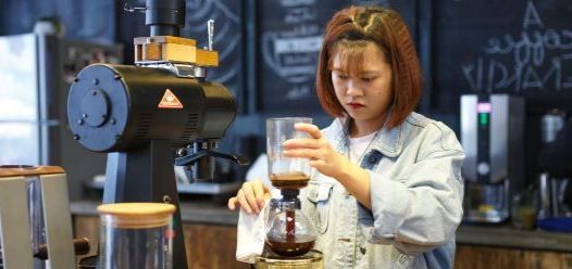 Female barista at work filtering coffee in front of a blackboard