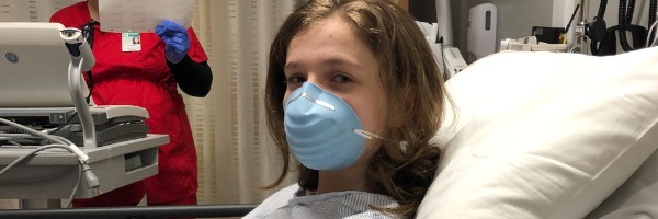 A young patient in a hospital bed wearing a face mask