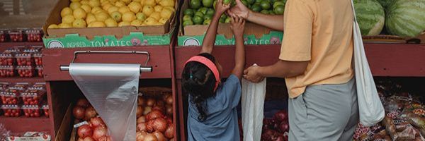 A young child and adult picking fruit from a stall