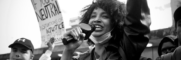 A person speaking into a microphone surrounded by people holding signs