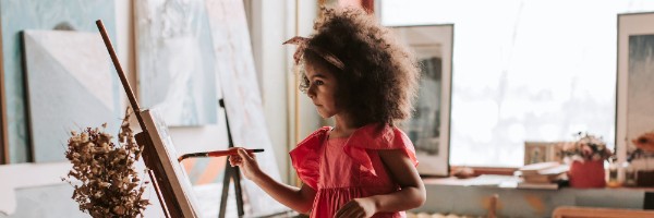 A child with afro hair painting on a easel 
