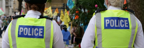 The backs of two Police Officers in Hi-Vis vests with 'Police' on the back