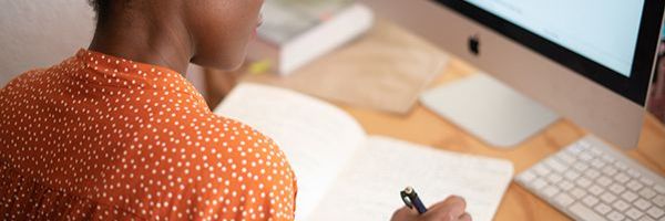 A person is writing in a notepad on a desk