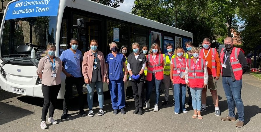 A group of vaccine volunteers wearing masks and standing in front of a vaccination bus